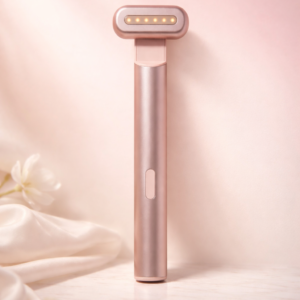 Rose gold 4 in 1 skincare wand with illuminated LED head, standing upright on a soft beige background with silk fabric and white flowers.